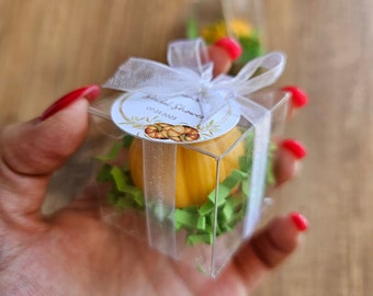 May include: A small clear box with a yellow pumpkin-shaped candle inside. The box is tied with a white ribbon and has a white tag that says "Bridal Shower" and "07.17.2023".