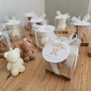 May include: A set of small, clear boxes with white ribbon and a brown teddy bear candle inside. Each box has a round sticker with a brown teddy bear and the text "Thank you, Carla's Baby Shower, June 1st, 2025".