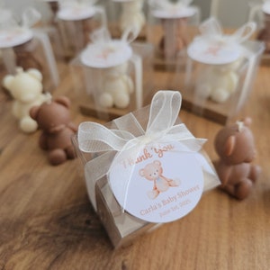 Puede incluir: Un conjunto de peque&ntilde;as cajas transparentes con lazos de cinta blanca, cada una contiene una peque&ntilde;a figura de osito de peluche. Las cajas tienen una pegatina redonda con una ilustraci&oacute;n de osito de peluche y el texto "Gracias, Baby Shower de Carla, 1 de junio de 2023".