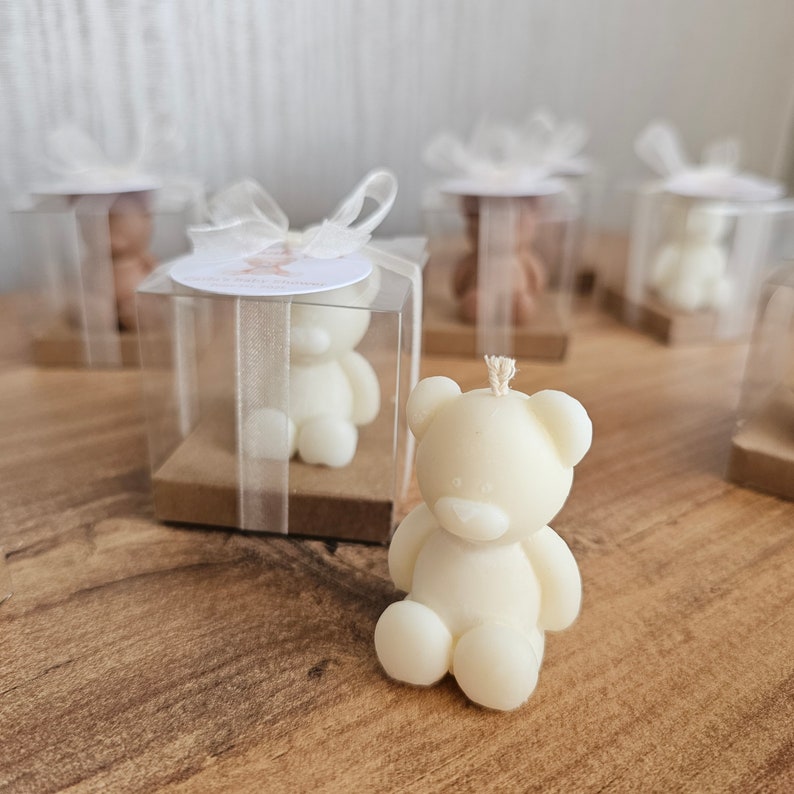 May include: A set of small white teddy bear candles in clear boxes with brown bases and white ribbon. The candles are perfect for a baby shower or birthday party.