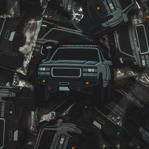 Könnte beinhalten: Nahaufnahme eines Stapels schwarzer und grauer Autoaufkleber. Die Aufkleber zeigen einen GMC-Truck mit schwarzer Frontstoßstange und silbernem Kühlergrill. Die Aufkleber befinden sich in Plastiktüten.