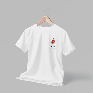 May include: White t-shirt with a small embroidered image of a soccer player wearing a red jersey and white shorts.