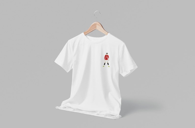 May include: White t-shirt with a small embroidered image of a soccer player wearing a red jersey and white shorts.