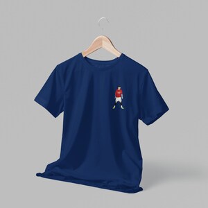 May include: A navy blue t-shirt with a small embroidered image of a soccer player wearing a red jersey, white shorts, and green socks.