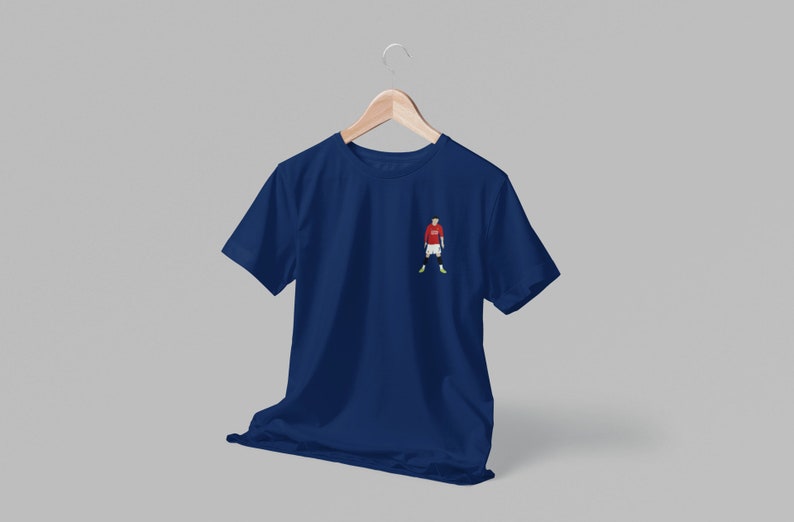 May include: A navy blue t-shirt with a small embroidered image of a soccer player wearing a red jersey, white shorts, and green socks.