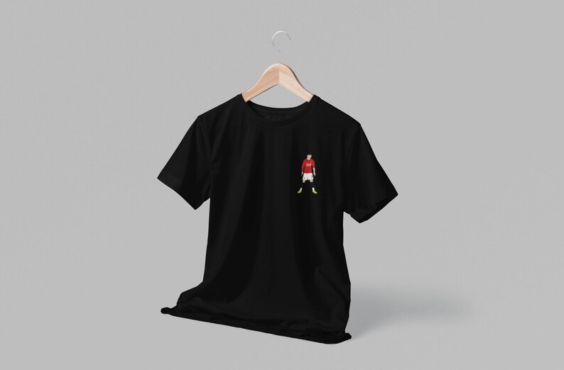 May include: Black t-shirt with a small embroidered image of a soccer player wearing a red jersey, white shorts, and yellow socks.