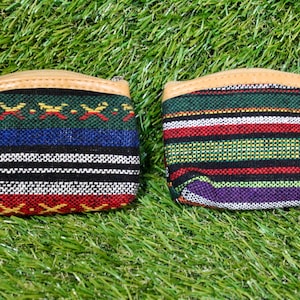 May include: Two small, colorful coin purses with a woven fabric design. One purse features a pattern of red, blue, and white stripes, while the other has green, red, and purple stripes. Both have a tan leather top and zipper.