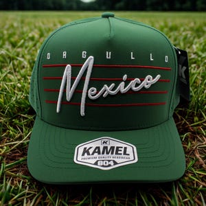 May include: A green baseball cap with the word "Mexico" embroidered in white script, accented by red stripes. The cap also features the word "ORGULLO" above the script and a "KAMEL" logo patch.