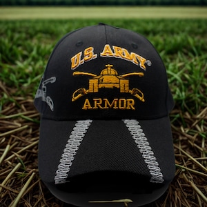 May include: Black baseball cap with embroidered gold text and a tank graphic. The text reads "U.S. ARMY ARMOR". The brim features a design of silver tank treads. A military-themed cap.