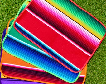 May include: Four colorful Mexican blankets stacked on top of each other. The blankets are striped with red, green, blue, orange, purple, and white.