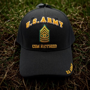Puede incluir: Gorra de béisbol negra con bordados dorados y verdes. La gorra presenta "U.S. ARMY" en dorado, una insignia verde y dorada y "CSM RETIRED" en dorado. Las palabras "U.S. ARMY" también están bordadas en el lateral.