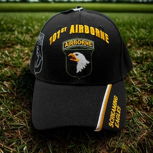 May include: Black baseball cap with the text "101st AIRBORNE" in yellow and a patch with an eagle. The cap also features the words "SCREAMING EAGLES" in yellow and white on the side.