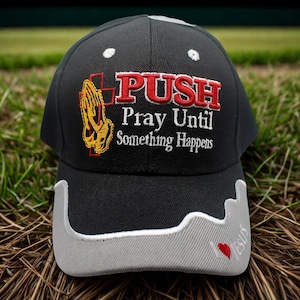 May include: Black baseball cap with the embroidered text "PUSH Pray Until Something Happens". The cap features a gray brim with a white outline and a small red heart. The cap has white stitching on the top.