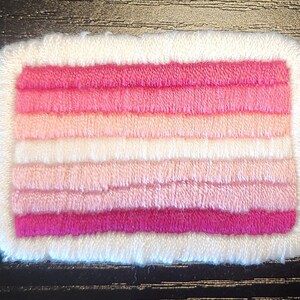 Op de afbeelding: Een rechthoekige patch met een witte rand en een ontwerp van horizontale strepen in verschillende roze tinten. De strepen variëren van lichtroze tot een diep magenta, waardoor een gradiënteffect ontstaat. De patch heeft een getextureerde, geborduurde uitstraling.