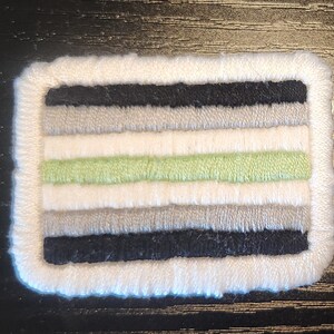 May include: Embroidered rectangular patch featuring a white border and horizontal stripes in black, grey, white, and light green. The patch has a textured finish, designed for application to fabric.