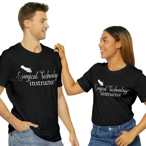 May include: Two people wearing black t-shirts with the text "Surgical Technology Instructor" and a white illustration of a hand holding a surgical tool.