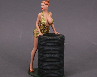 May include: A gold glitter dress figurine of a woman leaning against a stack of five black tires.