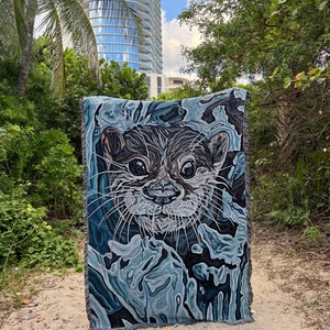 May include: A woven tapestry featuring a close-up of an otter's face with a blue and gray abstract background.
