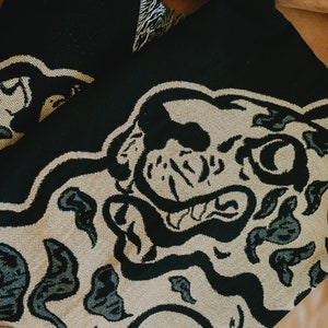 May include: Black and beige woven throw blanket with a large black and white animal print design. The animal's face is prominent in the design.