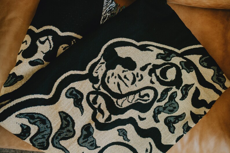 May include: Black and beige woven throw blanket with a large black and white animal print design. The animal's face is prominent in the design.