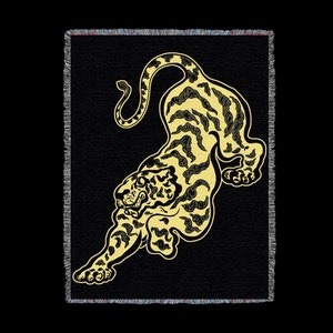 May include: A black and gold woven tapestry featuring a stylized tiger design. The tiger is depicted in a leaping pose with its head turned to the side. The tapestry has a fringed border.