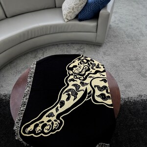 May include: Black throw blanket with a gold embroidered jaguar design. The blanket has fringe around the edges.