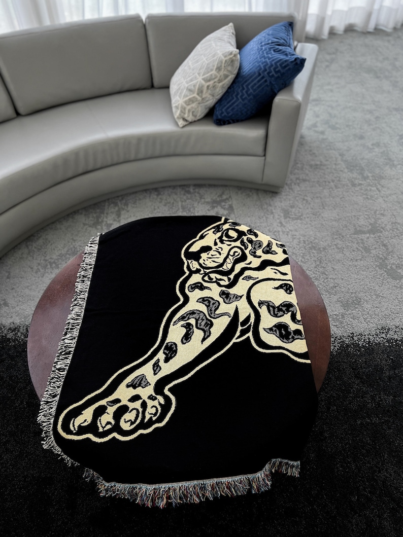 May include: Black throw blanket with a gold embroidered jaguar design. The blanket has fringe around the edges.