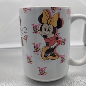 Pu&ograve; includere: Tazza in ceramica bianca con un design Minnie Mouse rosa e giallo. La tazza presenta un motivo ripetuto di Minnie Mouse e il logo Louis Vuitton.