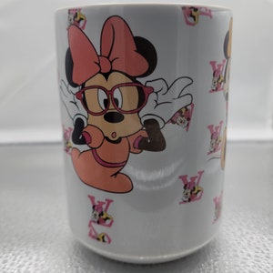 Pu&ograve; includere: Tazza in ceramica bianca con un design Minnie Mouse rosa e bianco. Minnie Mouse indossa occhiali rossi e un fiocco rosa. La tazza &egrave; decorata con un motivo ripetitivo di "V" rosa.