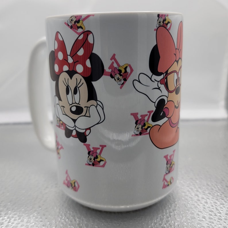 Pu&ograve; includere: Una tazza in ceramica bianca con un design rosa e rosso con personaggi di Topolino. La tazza ha un manico ed &egrave; decorata con un motivo ripetitivo di teste di Topolino e il logo Louis Vuitton.