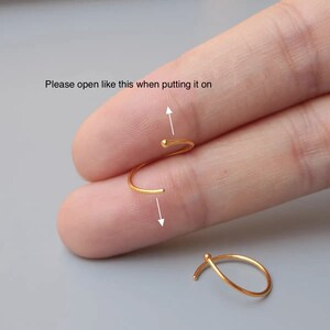 May include: A gold-colored earring with a curved design and a small ball at the end. The text in the image reads, "Please open like this when putting it on." The earring is shown being opened, with an arrow indicating the direction.