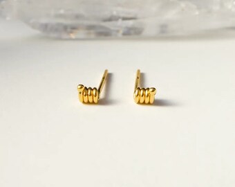 May include: A pair of gold-toned stud earrings with a coiled design. The earrings are small and delicate.