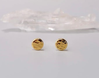 May include: A pair of gold hammered circle stud earrings. The earrings are small and delicate, and they have a textured surface.