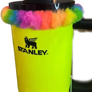 May include: A yellow Stanley travel mug with a black logo and a rainbow colored fuzzy band around the top.