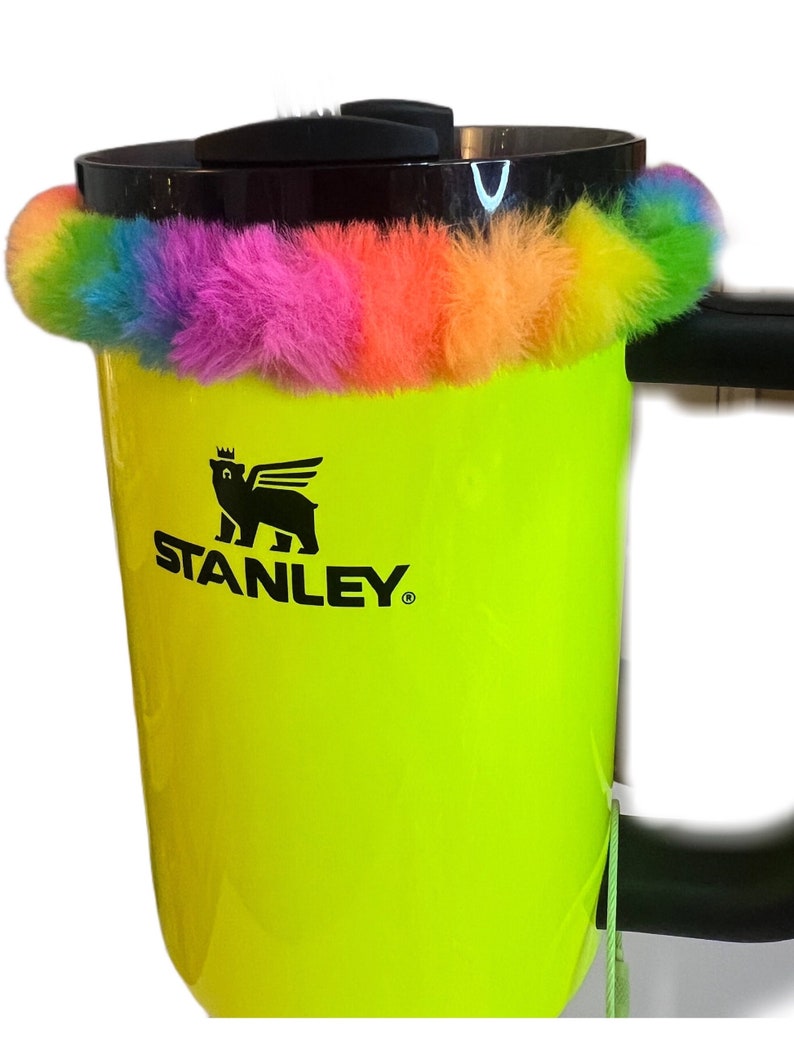 May include: A yellow Stanley travel mug with a black logo and a rainbow colored fuzzy band around the top.