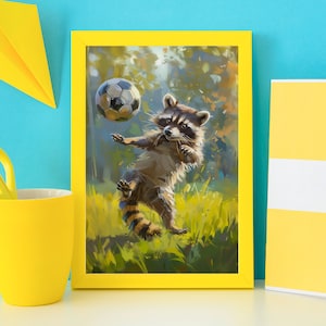 Op de afbeelding: Een ingelijste kunstdruk met een schilderij van een wasbeer die met een zwart-witte voetbal in een grasveld speelt. De wasbeer heeft grijs en bruin bont met een gestreepte staart. De lijst is felgeel en heeft een rechthoekige vorm.