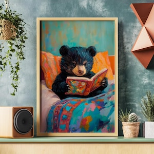 May include: A black bear cub wearing a colorful blanket sits in a bed and reads a book with a bright, colorful cover.
