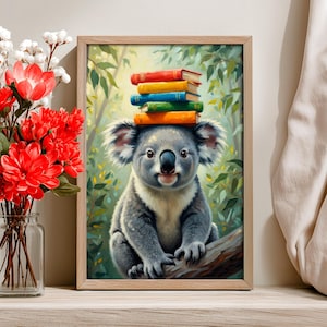 May include: A framed print featuring a koala sitting on a branch with a stack of colorful books balanced on its head. The koala has gray fur, a black nose, and a smiling expression. The background shows a lush green forest.