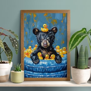 May include: A framed art print featuring a black bear cub in a blue tub surrounded by yellow rubber duckies. The bear has a yellow duck on its head. The background is blue with orange paint splatters. The artwork is in a wooden frame.