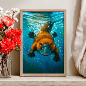 May include: A framed art print featuring a vibrant illustration of a platypus swimming underwater. The platypus has brown fur and a blue bill, set against a blue water background with bubbles and green aquatic plants. The artwork is in a wooden frame.