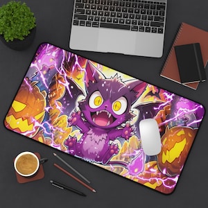 Op de afbeelding: Een rechthoekige muismat met een cartoon paarse kat met vleermuisvleugels, omringd door pompoenen en vleermuizen. Het ontwerp heeft een Halloween-thema met gele, oranje en paarse kleuren. Een computermuis ligt op de mat.