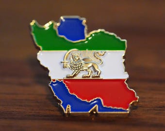 May include: A colorful enamel pin in the shape of a map, featuring green, white, red, and blue sections. A gold lion emblem is centered on the white portion. The pin is set against a dark wood surface.