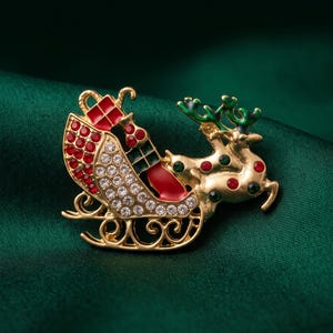 May include: A gold-tone metal brooch shaped like a reindeer pulling a sleigh. The sleigh is decorated with clear rhinestones and red enamel accents. The reindeer features green enamel antlers and is adorned with small red and green circular stones.