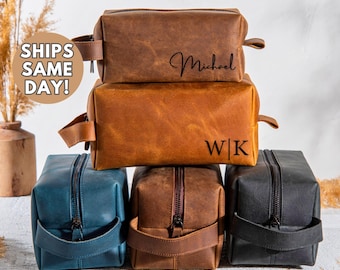 May include: Four leather toiletry bags in different colors. The top bag is brown with the name "Michael" written on it. The second bag is brown with the initials "W|K" written on it. The third bag is blue and the fourth bag is black.
