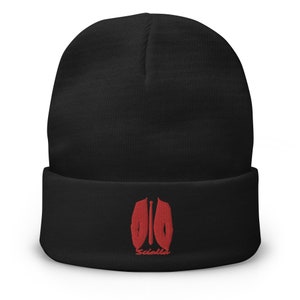 Pode incluir: Gorro preto com um design bordado vermelho de um terno e uma gravata com a palavra "Saicolle" embaixo.