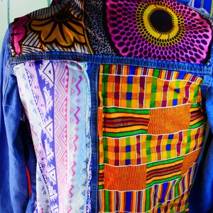 May include: A blue denim jacket with colorful patterned fabric patches. The patches feature geometric designs in shades of pink, yellow, blue, green, and orange.
