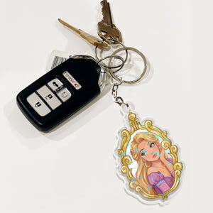 May include: A clear acrylic keychain featuring a cartoon image of a woman with long blonde hair, in a gold ornate frame. The keychain is attached to a set of keys and a black car key fob.
