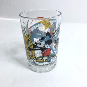 May include: A clear glass tumbler featuring a colorful graphic of Mickey Mouse at a ship's wheel. The design includes yellow, red, and blue accents with printed text such as Mickey Mouse 1928's Steamboat Willie and Donald's middle name is Fauntleroy.