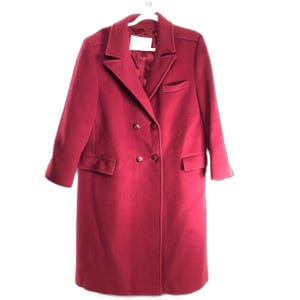 May include: A deep magenta double-breasted coat featuring a notched lapel collar, long sleeves, and two front flap pockets. The coat includes a single chest welt pocket and four visible buttons on the front closure, finished with a smooth lining.