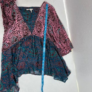 Op de afbeelding: Een top met patroon met een V-hals ontwerp. De top heeft een combinatie van roze en teal kleuren met ingewikkelde paisley patronen. Het kledingstuk heeft lange mouwen en een vloeiend, gelaagd silhouet, met een afmeting van ongeveer 66 cm.
